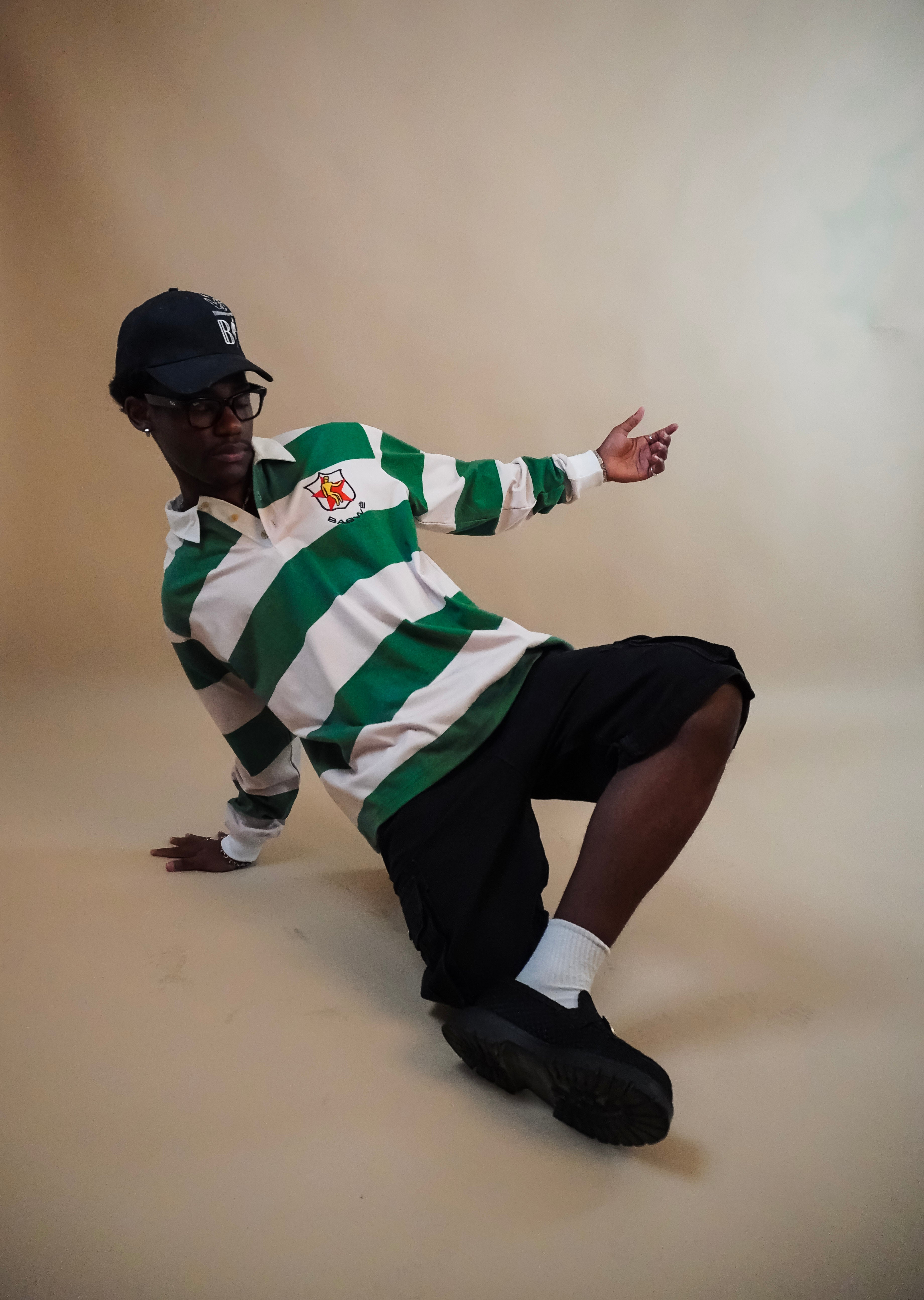 Person wearing a green and white striped  Zimbabwean rugby jersey with a cap, sitting on a beige background