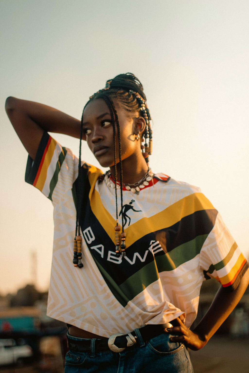 Woman wearing a colorful striped Authentic vintage Zimbabwe football jersey with bold green, gold, red, and black details, celebrating 90s Zimbabwean soccer heritage, outdoors.